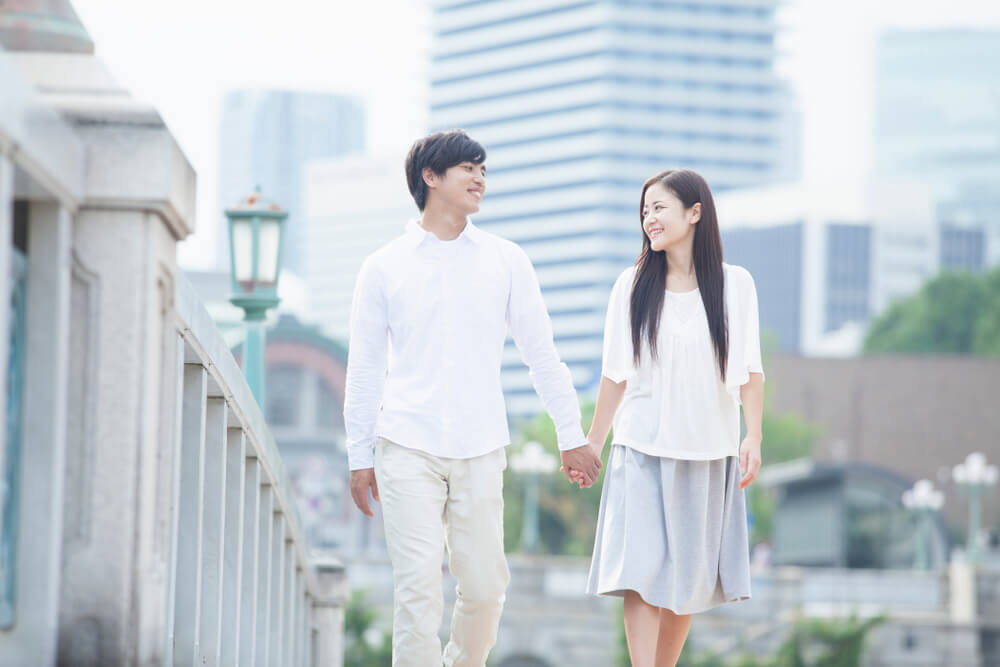 日本の街中を手をつないで歩くアジア系カップル
