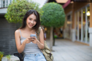 スマートフォンを持ちながら、こちらを向いてはにかむ東南アジアの女性