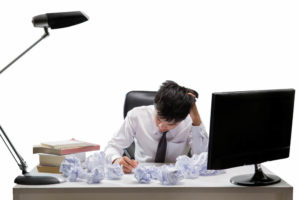 デスクの上に書類のゴミが山のように溜まって頭を抱えている男性