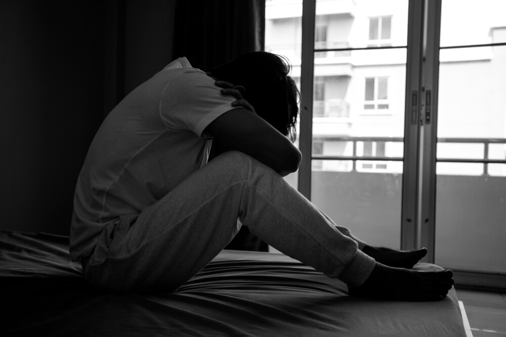 離婚時に跛行婚になってしまい、空っぽになった部屋のベッドでうずくまる若いアジア人男性