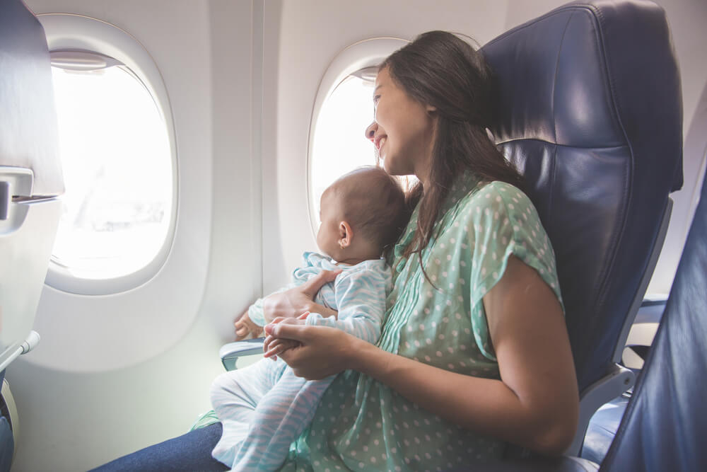 お母さんの膝上に座って飛行機に乗る赤ちゃん