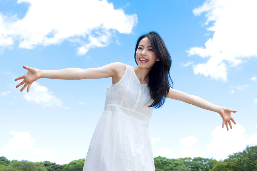 清潔感ある真っ白なワンピースを着て両手を広げたアジア人女性