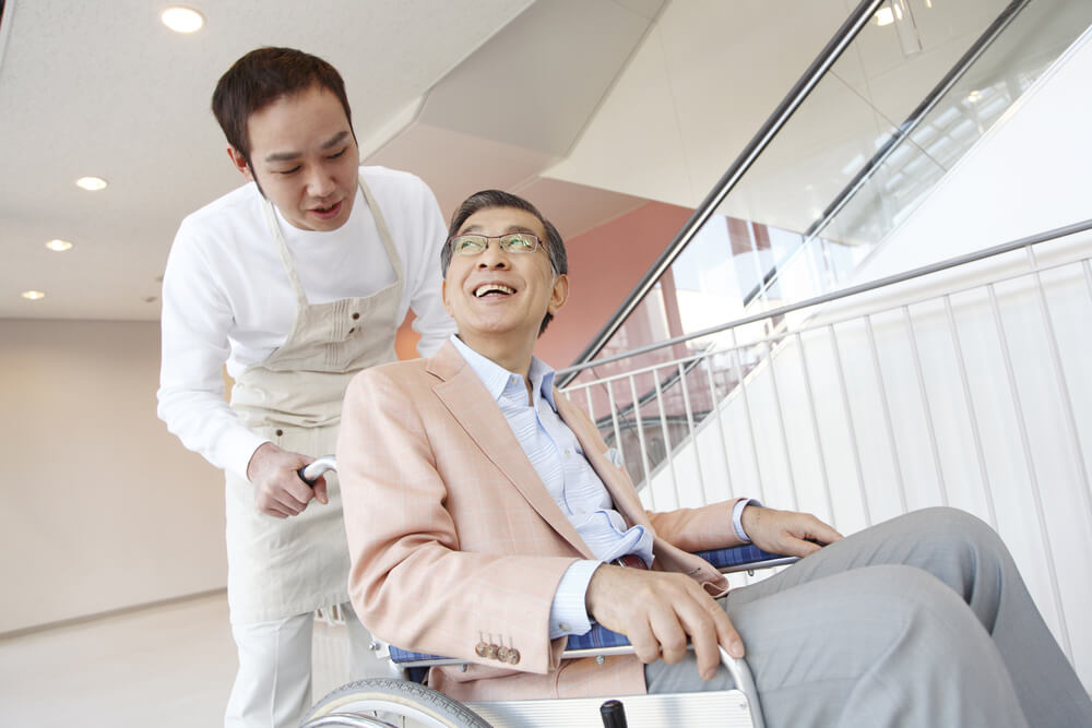 アジア人の若者介護士が、車いすの日本人男性を介護している