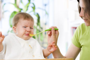 ぐずる赤ちゃんに、笑顔でご飯をあげる外国人女性
