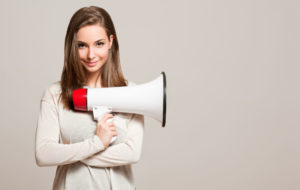 メガホンを手に持った女性が、こちらに笑みを投げかけている