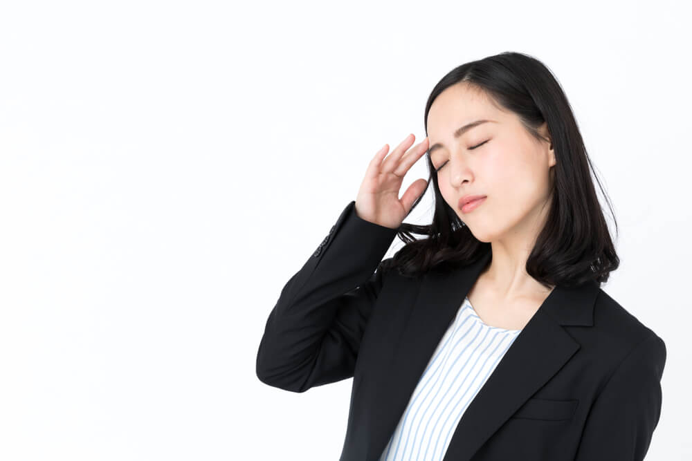 こめかみをおさえて悩む、リクルートスーツ姿のアジア人女性