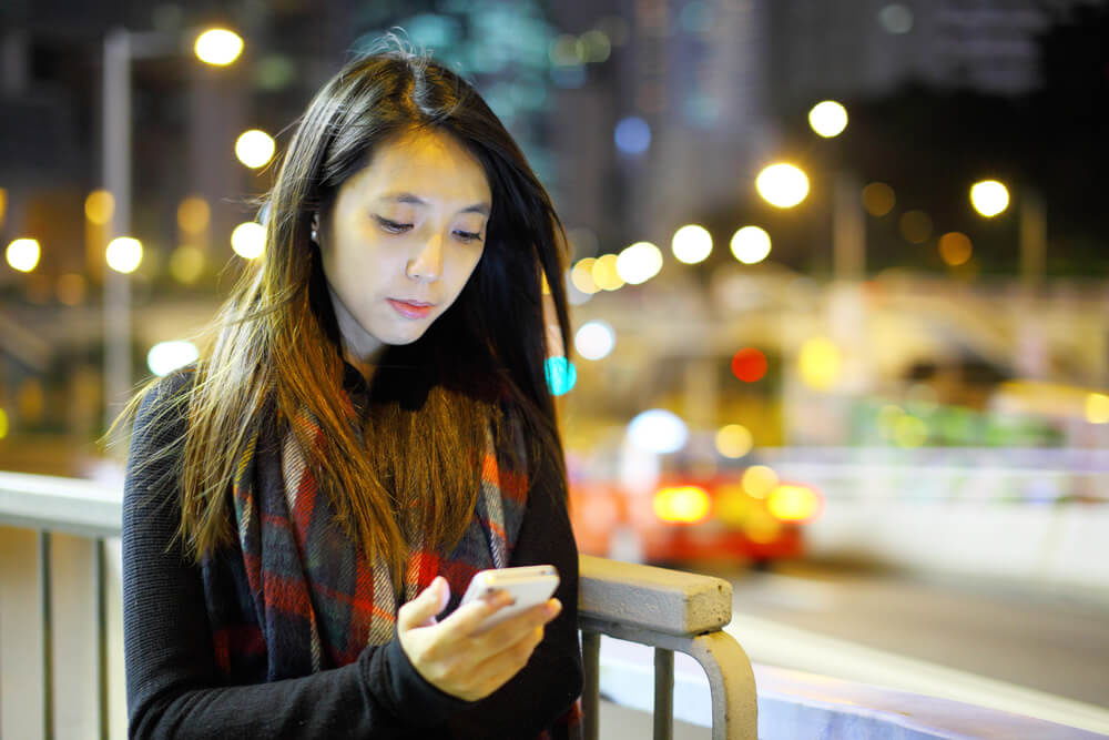 夜の街で暗い表情でスマホをいじる中国人女性